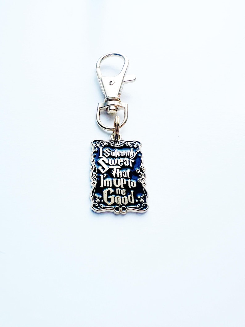 May include: A silver keychain with a rectangular charm. The charm features the text "I Solemnly Swear That I'm Up to No Good" on a black background. The charm is edged in silver with decorative flourishes.
