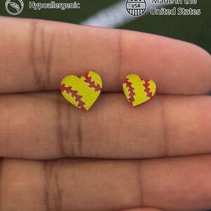 Fingers holding softball heart stud earrings