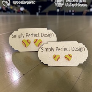 Two sizes of softball heart stud earrings on cards in a gym