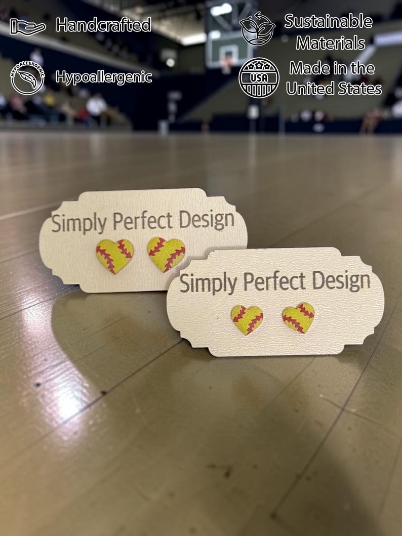 Two sizes of softball heart stud earrings on cards in a gym