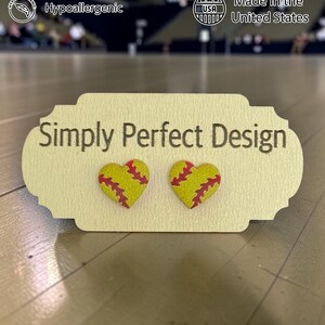 Large softball heart studs with red stitching on a card