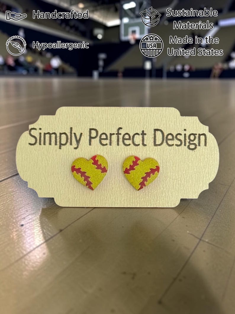 Large softball heart studs with red stitching on a card