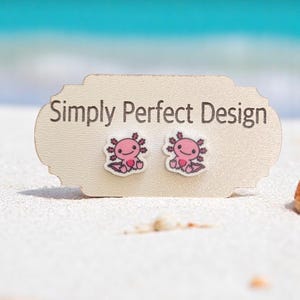 May include: A pair of pink axolotl stud earrings on a white card with the text "Simply Perfect Design".