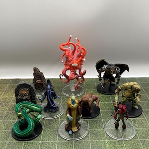 May include: A collection of fantasy miniature figures, including a red, tentacled creature, a winged demon, and various other monsters. The figures are on clear bases, set against a green and white grid background.