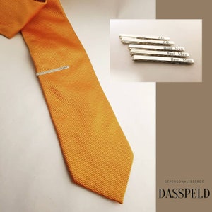 May include: A set of five silver tie clips with personalized engravings. The engravings include "J.G." and "Best Man". The tie clips are displayed on a white background.