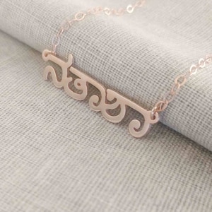 May include: A rose gold necklace with a delicate chain and a personalised nameplate featuring the word "Neera" in a cursive script.