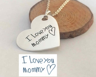 Puede incluir: Collar de plata en forma de corazón con un mensaje escrito a mano que dice "Te quiero mamá" con un corazón dibujado al lado.