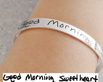 May include: A silver bracelet with the inscription "Good Morning Sweetheart" engraved on it.