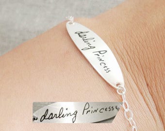 May include: A silver bracelet with a delicate chain and an oval charm engraved with the words "darling princess" in cursive handwriting.