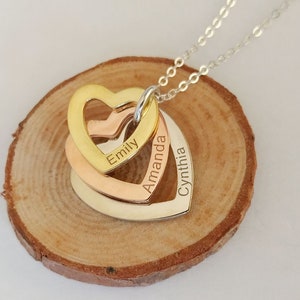 Puede incluir: Un collar de cadena de plata con tres colgantes de corazón entrelazados. Los corazones son de oro, oro rosa y plata. Cada corazón tiene un nombre grabado: Emily, Amanda y Cynthia.