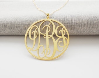 Puede incluir: Un collar de oro con un gran colgante redondo que presenta un monograma de tres letras en una fuente de escritura.