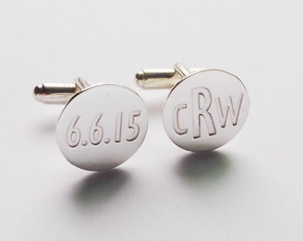 May include: A pair of silver cufflinks with engraved designs. One cufflink has the date "6.6.15" engraved on it, and the other cufflink has the initials "CRW" engraved on it.