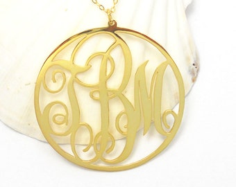 Puede incluir: Collar dorado con un colgante circular que presenta un monograma de las letras "R" y "M" en una fuente de letra decorativa.