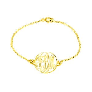 Könnte beinhalten: Ein goldenes Kettenarmband mit einem runden Anhänger mit einem Monogramm-Design. Der Anhänger ist ausgeschnitten und zeigt den Hintergrund.