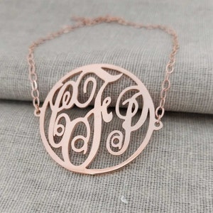 Könnte beinhalten: Eine Halskette aus Roségold mit einem runden Anhänger, der ein Monogramm der Buchstaben "B", "J" und "P" in kursiver Schrift zeigt.