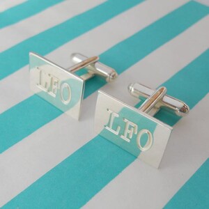 May include: A pair of silver cufflinks with a rectangular shape. Each cufflink has the letters "LFO" engraved on the front.
