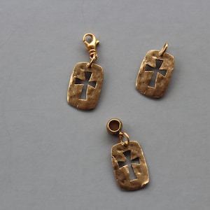 Pode incluir: Três pingentes de metal dourado com um design de cruz recortada. Os pingentes são retangulares e têm uma superfície texturizada.