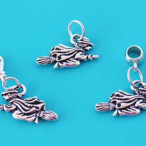 May include: Three silver charms of a witch flying on a broomstick. The charms are on a blue background.