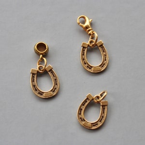 Pode incluir: Três pingentes de ferradura dourados. Dois dos pingentes estão presos a um anel dourado e o terceiro pingente está preso a um fecho dourado.