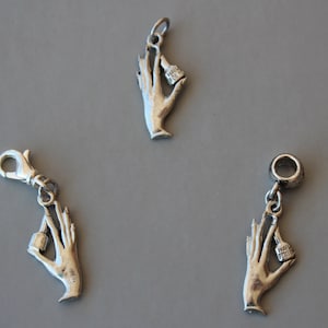 May include: Three silver charm bracelets with a hand holding a bottle of nail polish. The charms are attached to a silver chain.