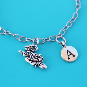 May include: A silver chain bracelet with a witch charm and a silver charm with the letter A.