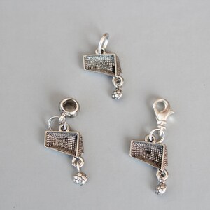 May include: Three silver charms in the shape of a soccer goal with a soccer ball hanging from the bottom.
