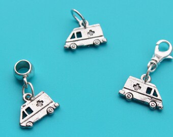 May include: Three silver charm pendants shaped like ambulances. The charms have a cross on the side and are on a blue background.