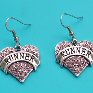 May include: A pair of silver heart-shaped earrings with pink rhinestones and the word "RUNNER" on a banner.