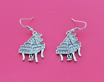 May include: A pair of silver earrings with a grand piano design. Each piano is decorated with clear rhinestones.