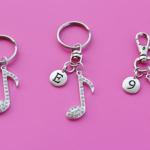May include: Three silver keychains with a music note charm. The charms are decorated with rhinestones. The first keychain has a charm with the letter "T" on it. The second keychain has a charm with the letter "E" on it. The third keychain has a charm with the number "9" on it.