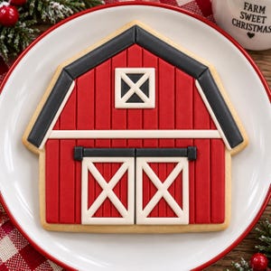 May include: A barn-shaped sugar cookie decorated with red icing for the walls, black icing for the roof and door trim, and white icing for the door and window cross-bracing details. The cookie features a central square window and two sliding doors.