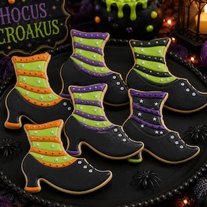 Puede incluir: Cinco galletas con forma de bota decoradas con glaseado negro en la parte inferior y glaseado verde a rayas en la parte superior. Las rayas están acentuadas con pequeñas estrellas blancas y puntos. Las galletas están sobre una bandeja negra.