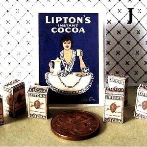 May include: A collection of miniature boxes of Lipton's Instant Cocoa. The boxes are brown with white lettering and feature a cocoa bean design. The boxes are arranged in a row on a white surface. There is a vintage advertisement for Lipton's Instant Cocoa in the background.