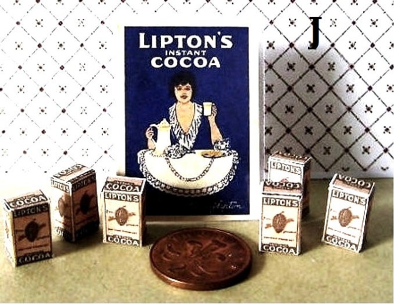 May include: A collection of miniature boxes of Lipton's Instant Cocoa. The boxes are brown with white lettering and feature a cocoa bean design. The boxes are arranged in a row on a white surface. There is a vintage advertisement for Lipton's Instant Cocoa in the background.