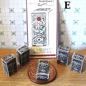 May include: A collection of six miniature boxes of Typhoo tea, with a vintage advertisement for the brand in the background. The boxes are black and white with gold lettering and feature the Typhoo logo. The advertisement reads "Beware of imitations! Typhoo Tea".
