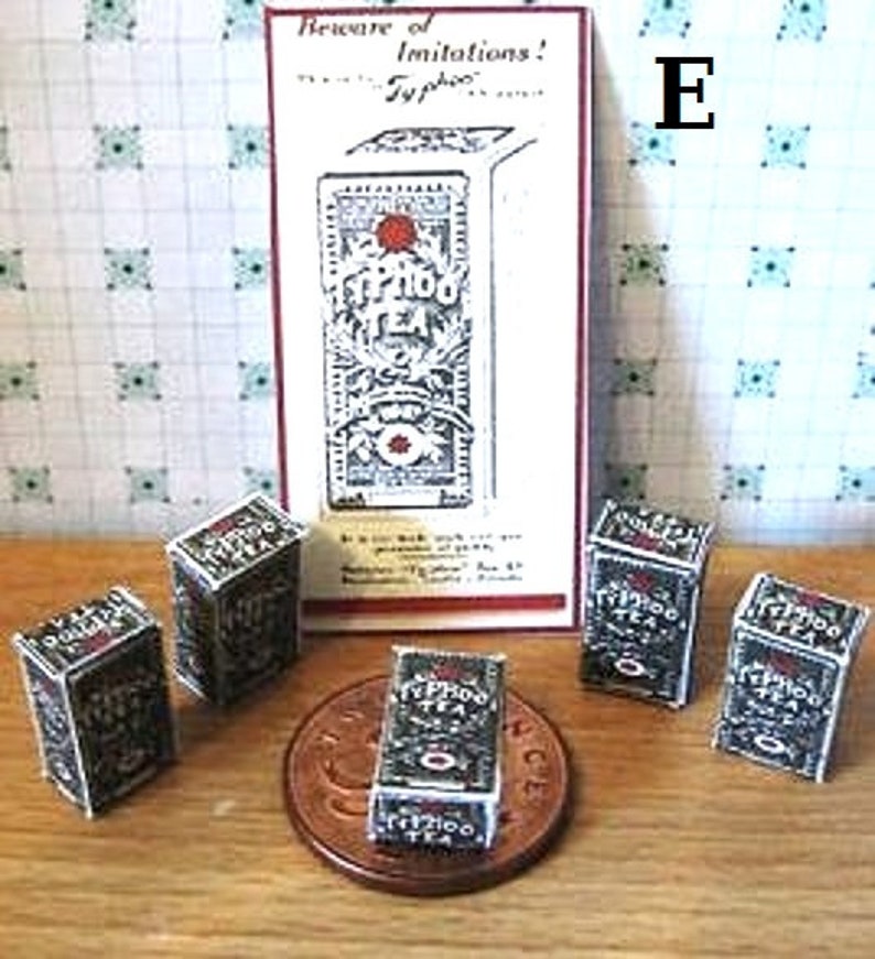 May include: A collection of six miniature boxes of Typhoo tea, with a vintage advertisement for the brand in the background. The boxes are black and white with gold lettering and feature the Typhoo logo. The advertisement reads "Beware of imitations! Typhoo Tea".