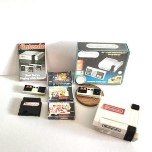 Könnte beinhalten: Miniatur-Nintendo Entertainment System-Set, einschließlich Konsole, Spielkassetten, Controllern und Verpackung. Die Verpackung lautet "Now You're Playing with Power!" und "Entertainment System". Die Konsole ist weiß und rot.