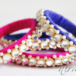May include: Set of four fabric bangles with a pink and blue color scheme. Each bangle is adorned with a row of round, clear glass stones set in gold-toned metal and white pearl accents.