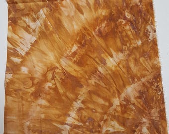 May include: A square piece of fabric featuring a tie-dye pattern in shades of golden brown, tan, and cream. The design displays diagonal streaks and organic, mottled textures across the surface, with raw, unfinished edges on all four sides.