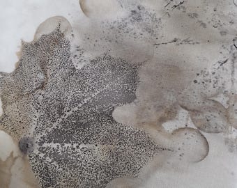 May include: A piece of off-white fabric featuring a botanical print with a prominent dark gray maple leaf silhouette. The design includes subtle, mottled brown and tan organic stains and speckles that create a textured, natural appearance.