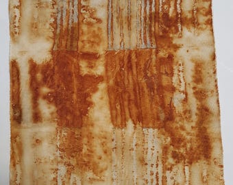 May include: A rectangular piece of off-white fabric featuring a rust-colored pattern. The design consists of vertical stripes and mottled, organic shapes in varying shades of burnt orange and brown, creating a textured, weathered appearance.