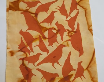 May include: A rectangular piece of fabric featuring a repeating pattern of solid orange bird silhouettes. The background is a light cream color with organic, swirling brown tie-dye or botanical-style stains throughout the entire surface.