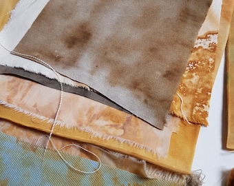 May include: A collection of layered fabric swatches featuring various textures and colors. The pieces include shades of mustard yellow, earthy brown, muted blue, and off-white, with some showing mottled, tie-dye, or botanical-style patterns.