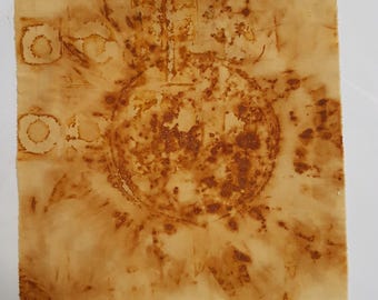 May include: A square piece of light beige fabric featuring a large, central circular rust-colored stain with a textured, mottled appearance. Smaller circular and rectangular rust-colored markings are visible along the left edge of the textile.