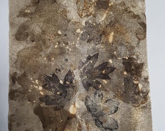 May include: A square piece of fabric featuring a botanical print with dark brown maple leaf silhouettes. The background is a mottled, textured beige and light brown surface with scattered cream-colored speckles and organic, earthy tones throughout.