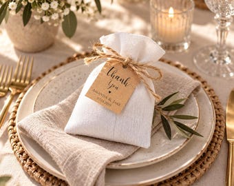 May include: A small white fabric drawstring pouch tied with brown twine and a rectangular kraft paper tag. The tag features the printed text "thank You" with a small heart icon, followed by "AMANDA & JAKE" and the date "03.14.2019" in black ink.