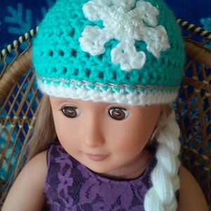 May include: A doll wearing a teal blue crocheted hat with a white snowflake design and a white crocheted braid.