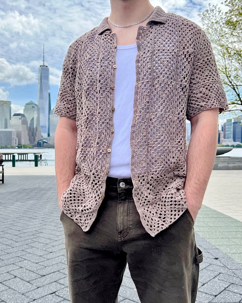 May include: A brown crochet shirt with a button-up front and short sleeves. The shirt is worn over a white tank top and brown pants.