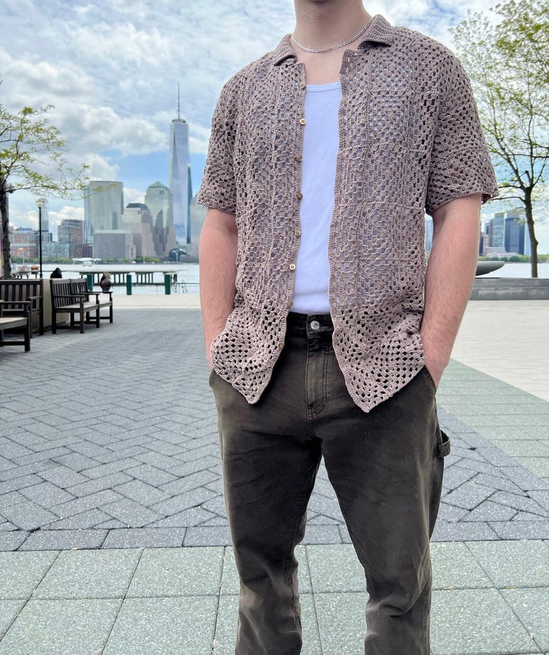 May include: A brown crocheted button-up shirt with short sleeves. The shirt is worn over a white tank top and brown pants.