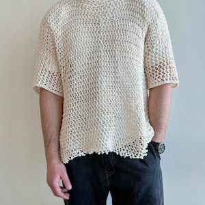 Könnte beinhalten: Ein weißes, gehäkeltes Shirt mit lockerer Passform und kurzen Ärmeln. Das Shirt hat einen ausgefransten, abgenutzten Saum.
